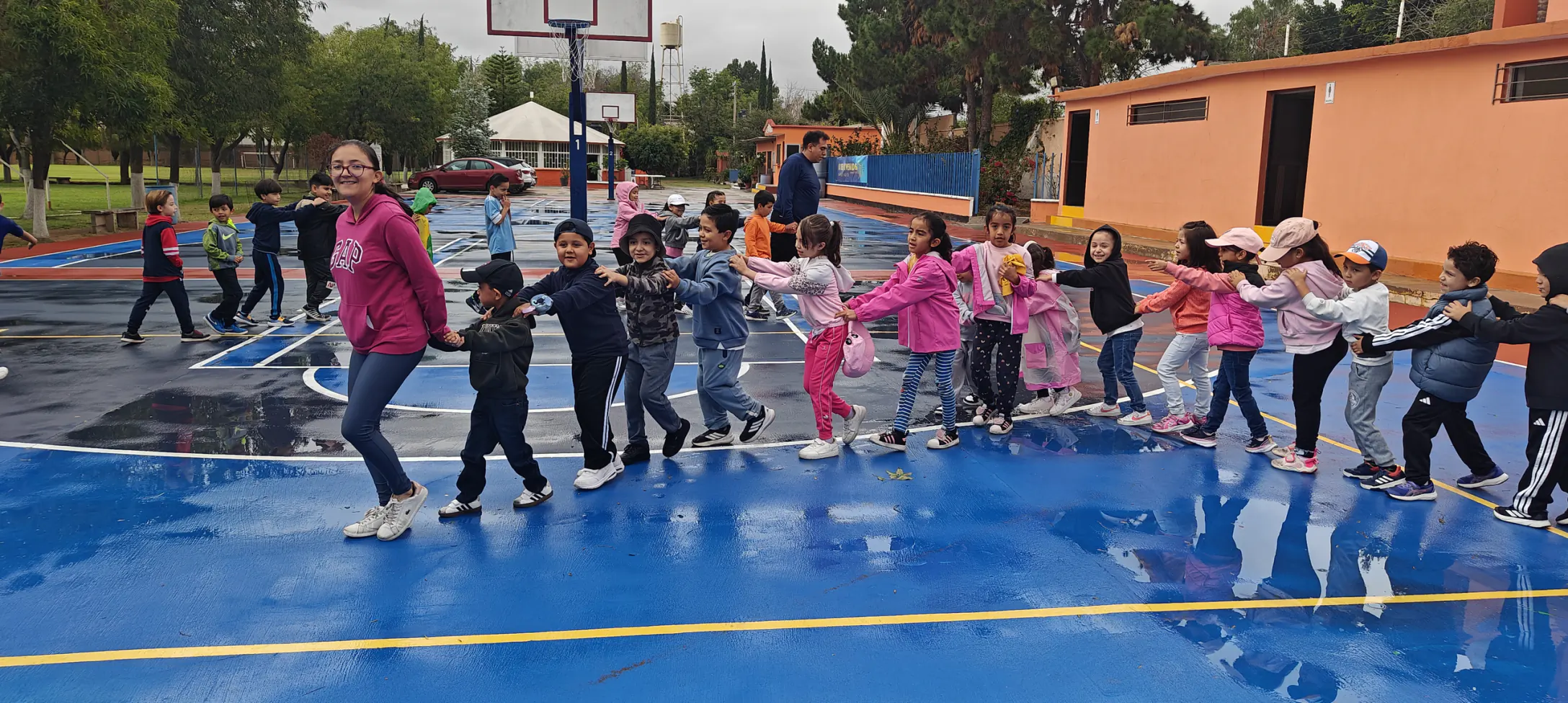 Niños de primaria menor en fila tomados de los hombros, jugando en la cancha