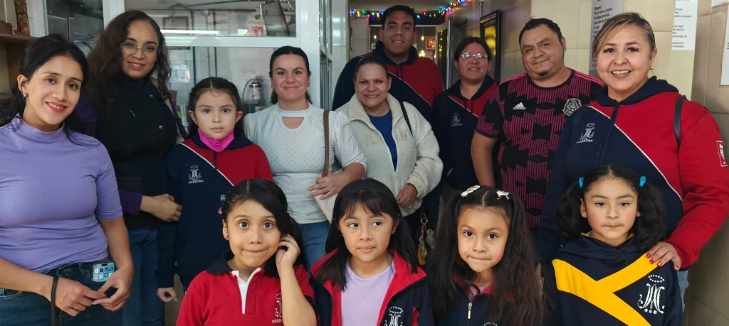 Madres y padres de familia con cuatro alumnas de primaria, sonriendo a cámara