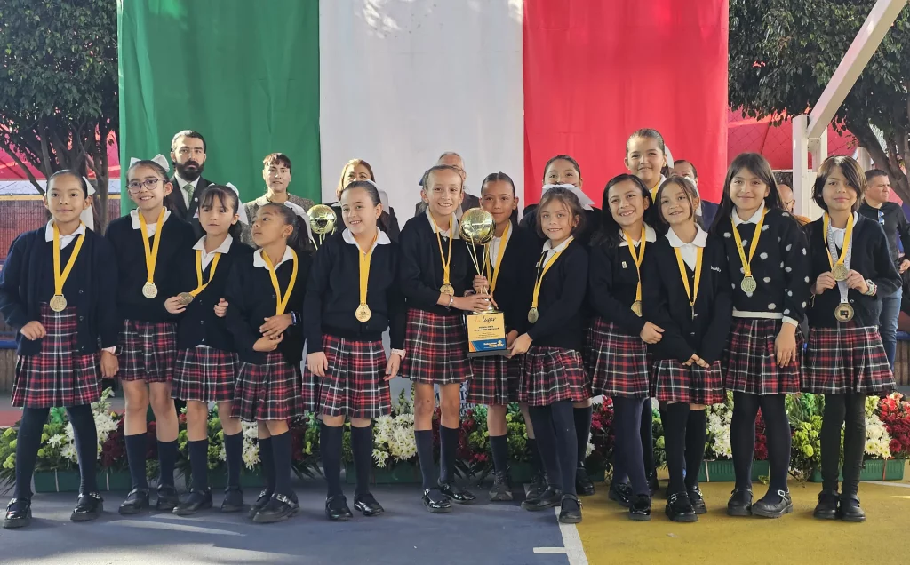 Equipo de alumnas con medallas y trofeo frente a la bandera