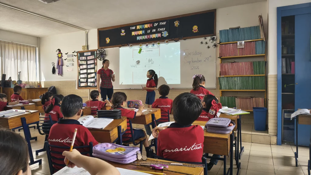 Clase de inglés con la maestra frente al pizarrón y los alumnos en sus mesas